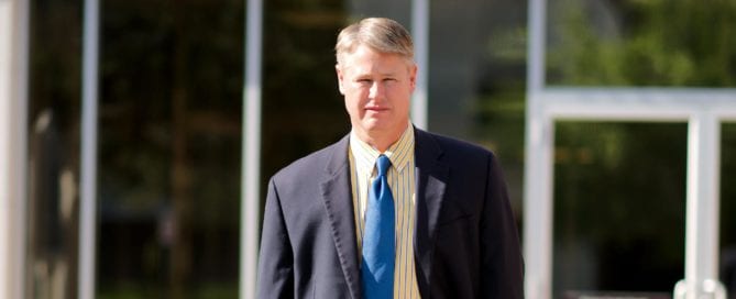 Man in a suit standing outdoors near a glass building in Madisonville Texas.