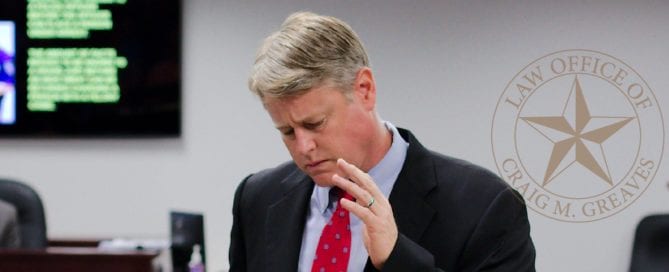 Man in a suit in a courtroom or office setting, looking down thoughtfully.