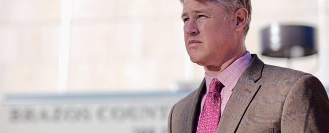 Man in a suit standing outdoors with a courthouse in the background.