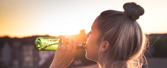 Young woman with a bun drinking from a green bottle at sunset.