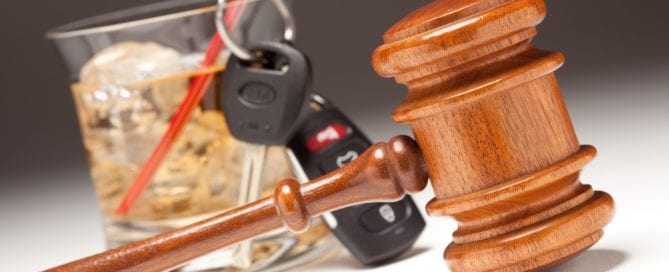 Gavel, car keys, and a drink with ice on a gray background.