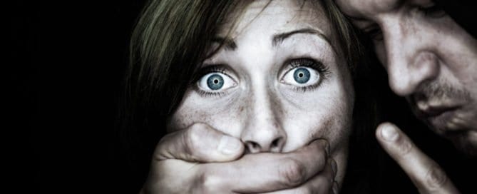 Woman with wide eyes being silenced by a man covering her mouth.