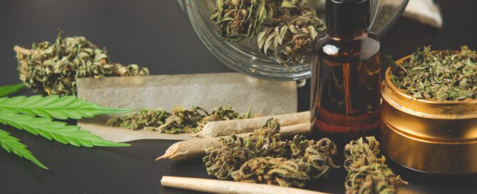 Cannabis buds, rolling papers, and a dropper bottle on a black surface.